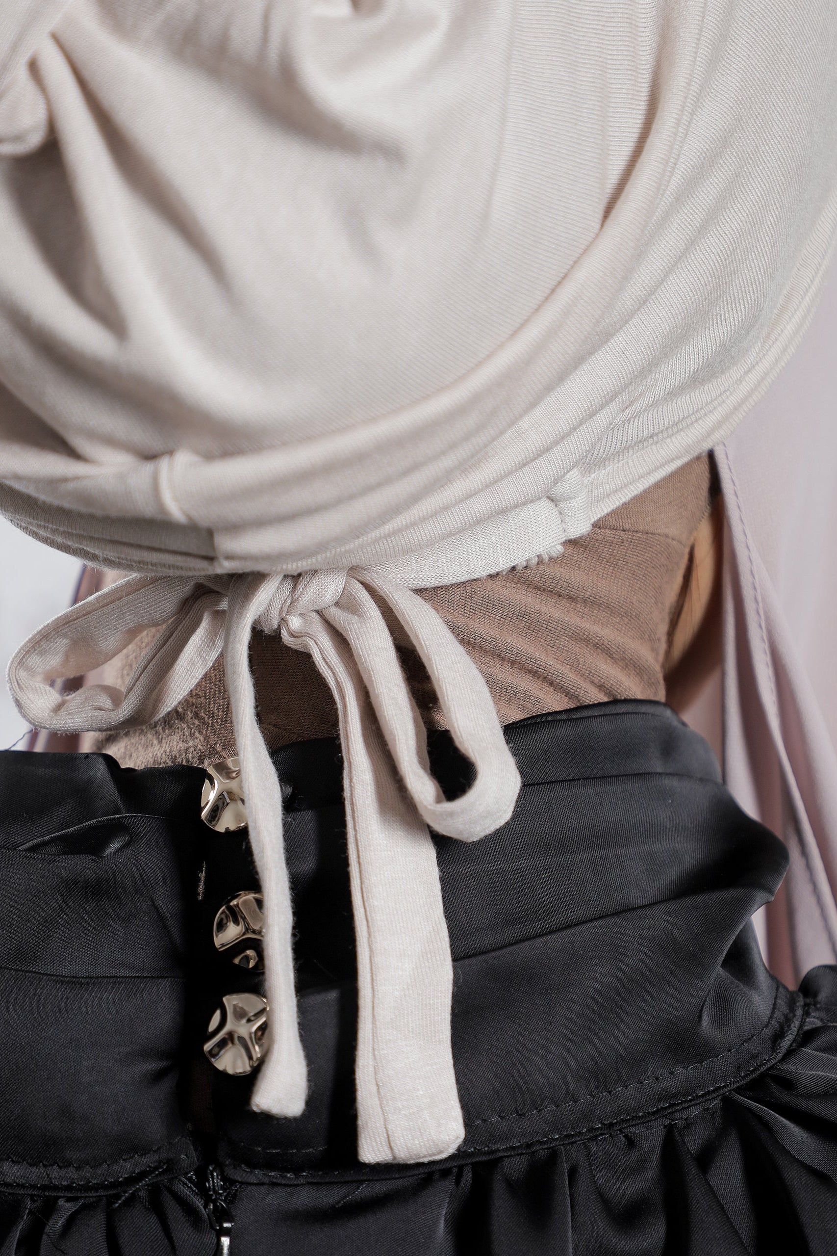 Close-up of a person wearing a beige hijab and black outfit with gold buttons.