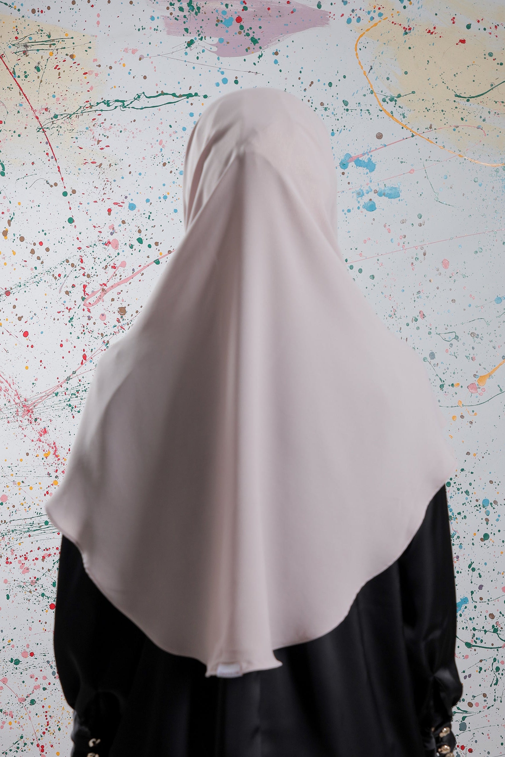 Person wearing a beige hijab against a colorful abstract background