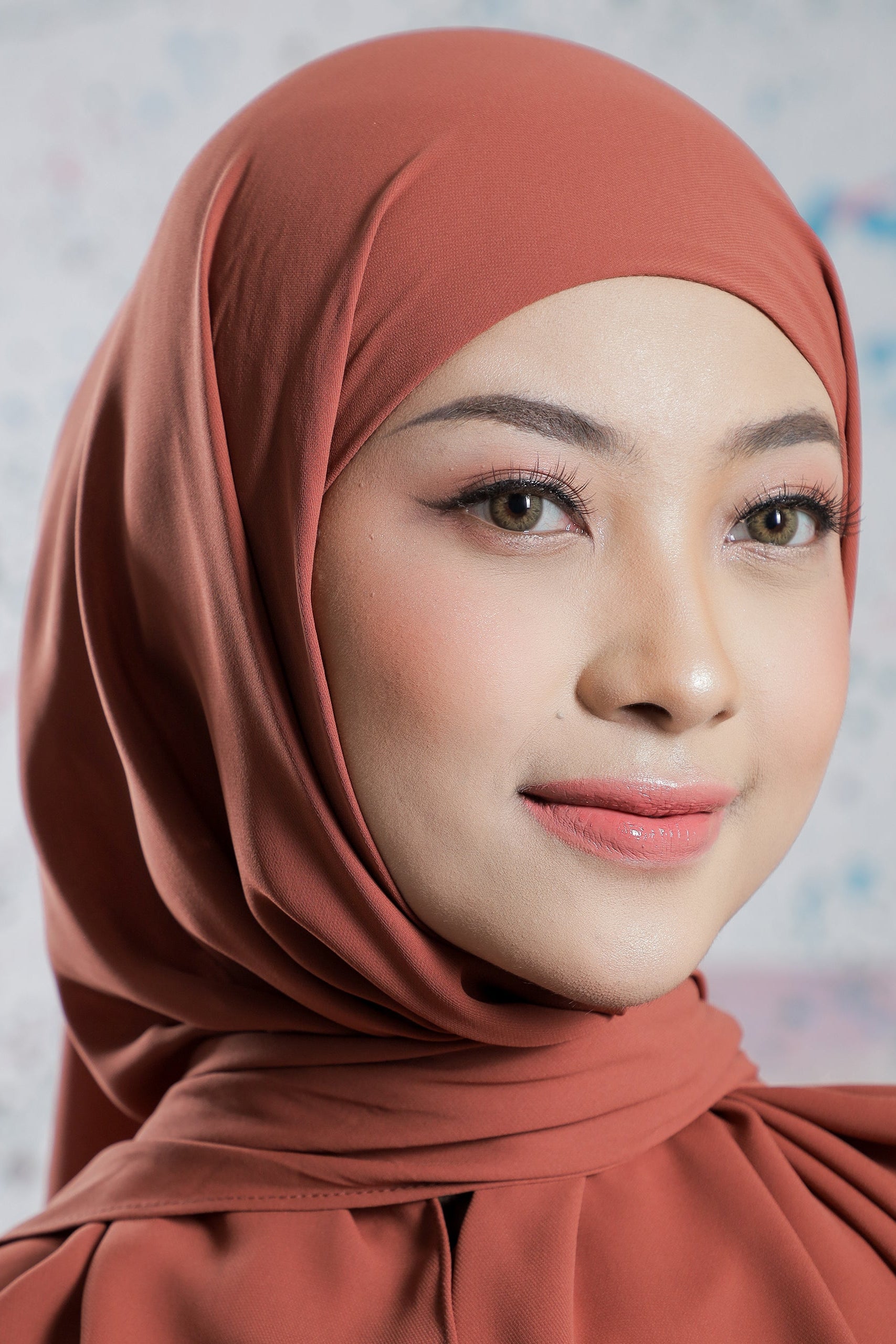 Woman wearing a brown hijab against a light background