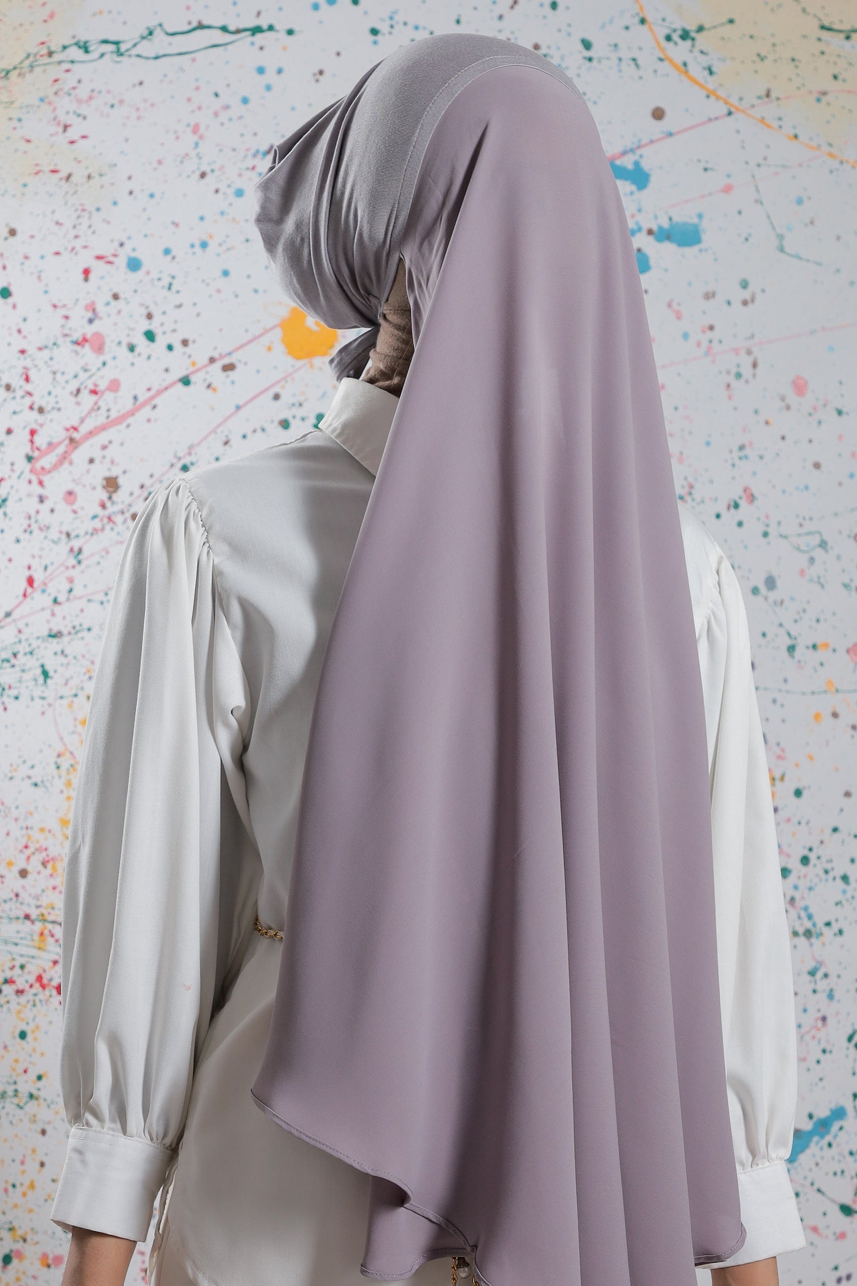 Person wearing a light purple hijab and white shirt against a colorful abstract background