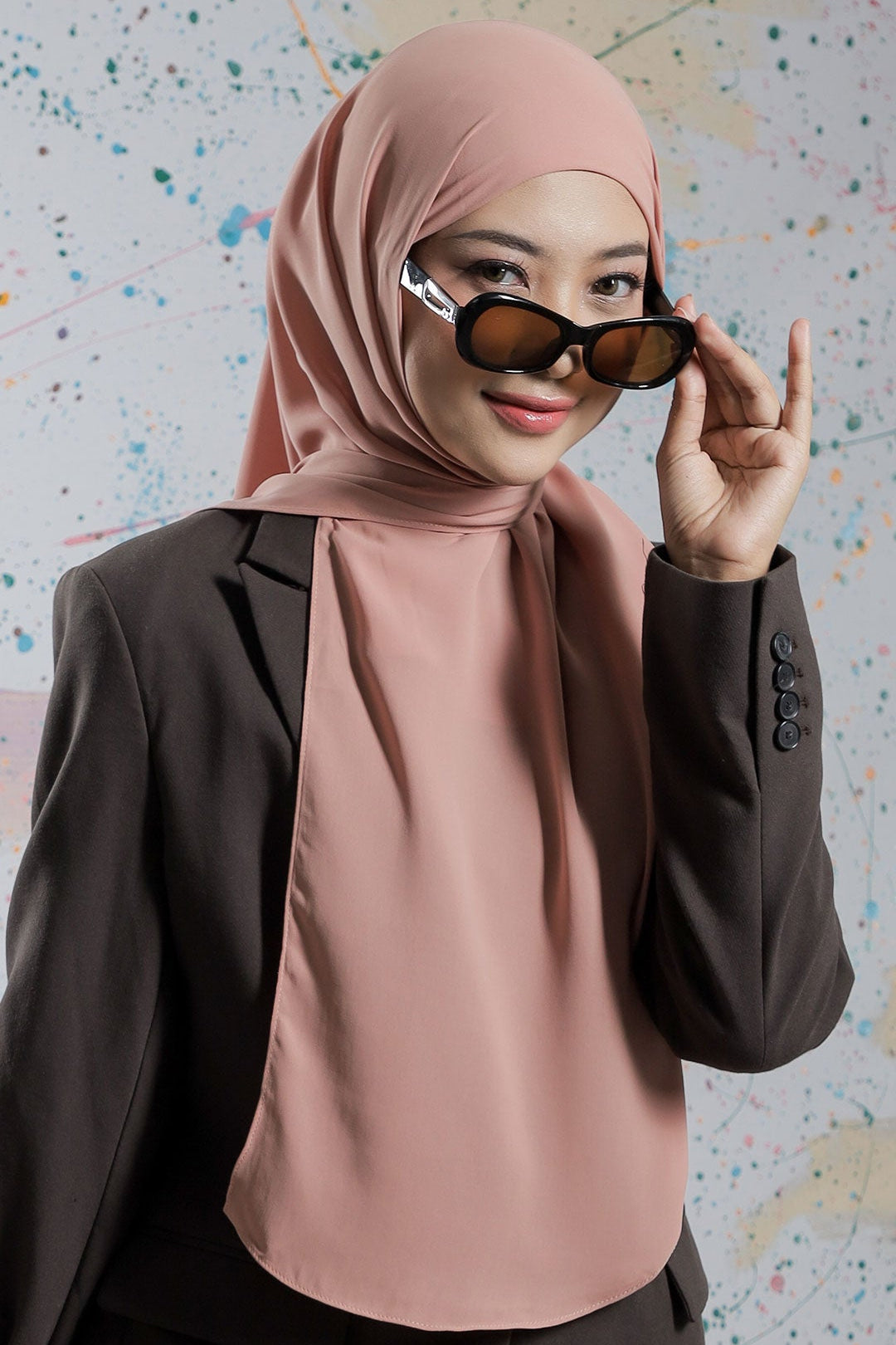 Woman wearing a pink hijab and sunglasses against a colorful abstract background