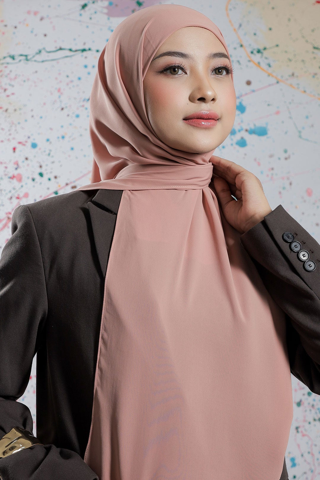 Woman wearing a pink hijab and black blazer against a colorful abstract background