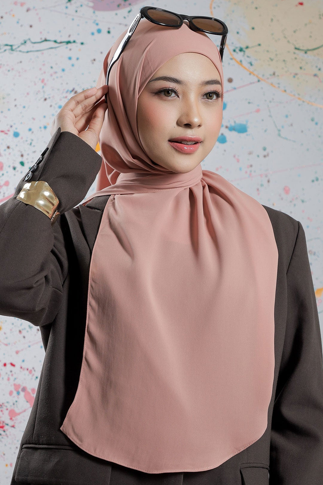 Woman wearing a pink hijab and dark blazer against a colorful abstract background