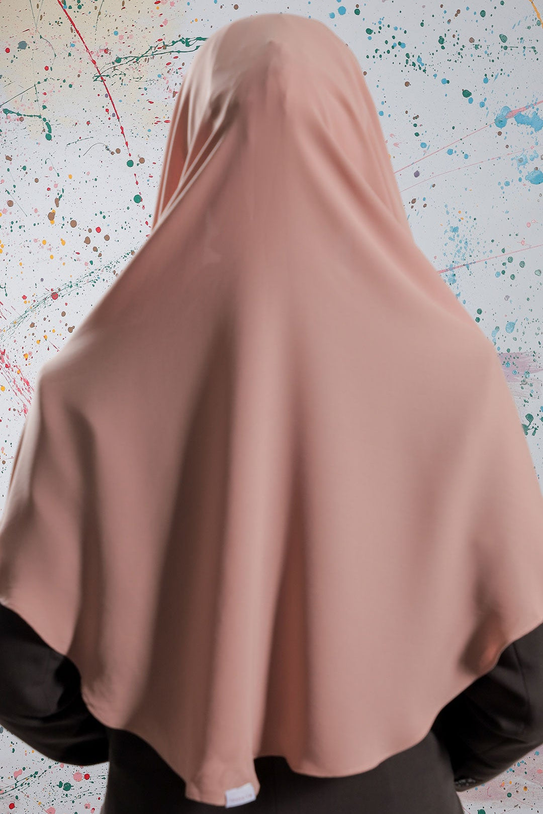 Person wearing a brown hijab against a colorful abstract background