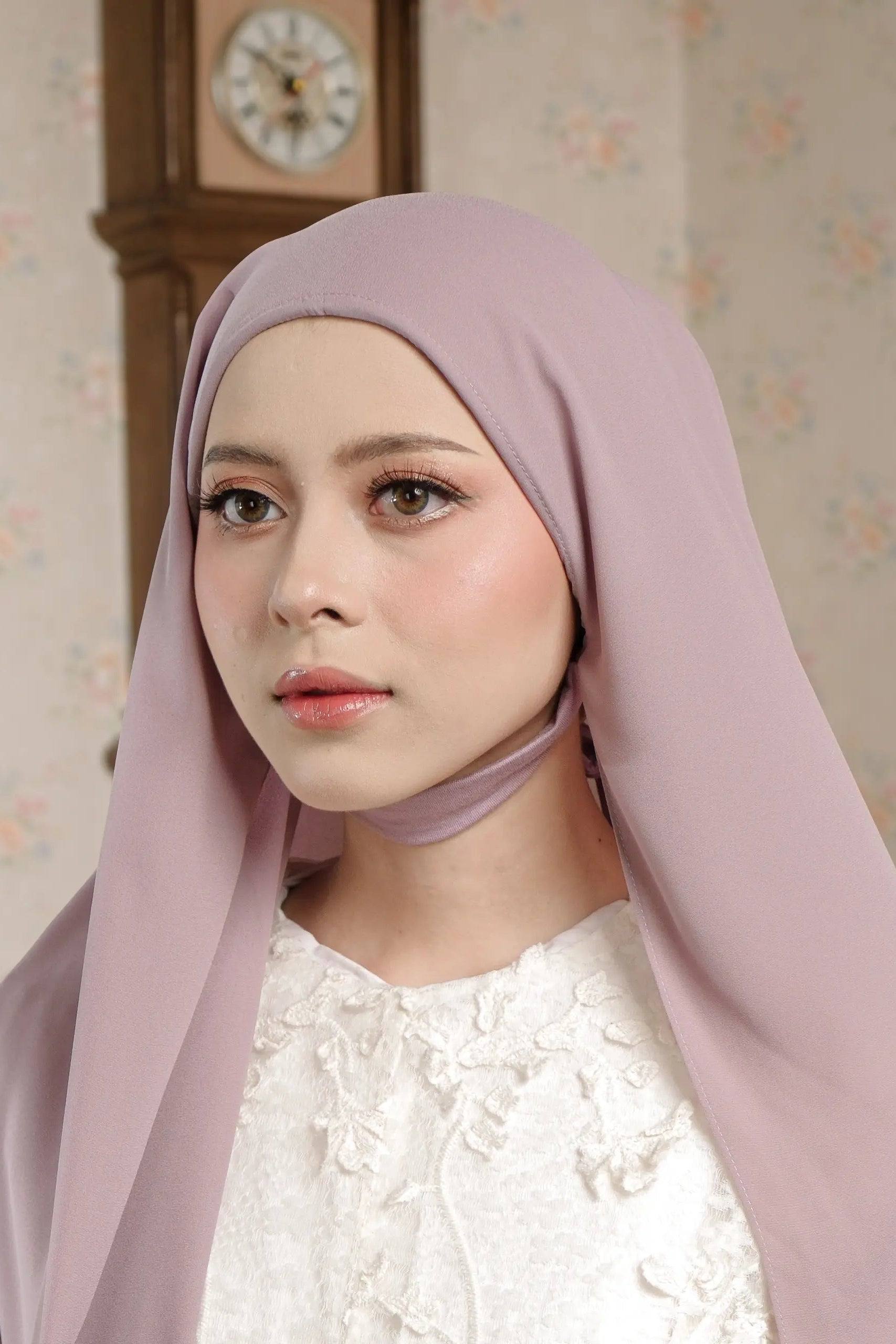 Woman wearing a light pink hijab with a decorative wall clock in the background