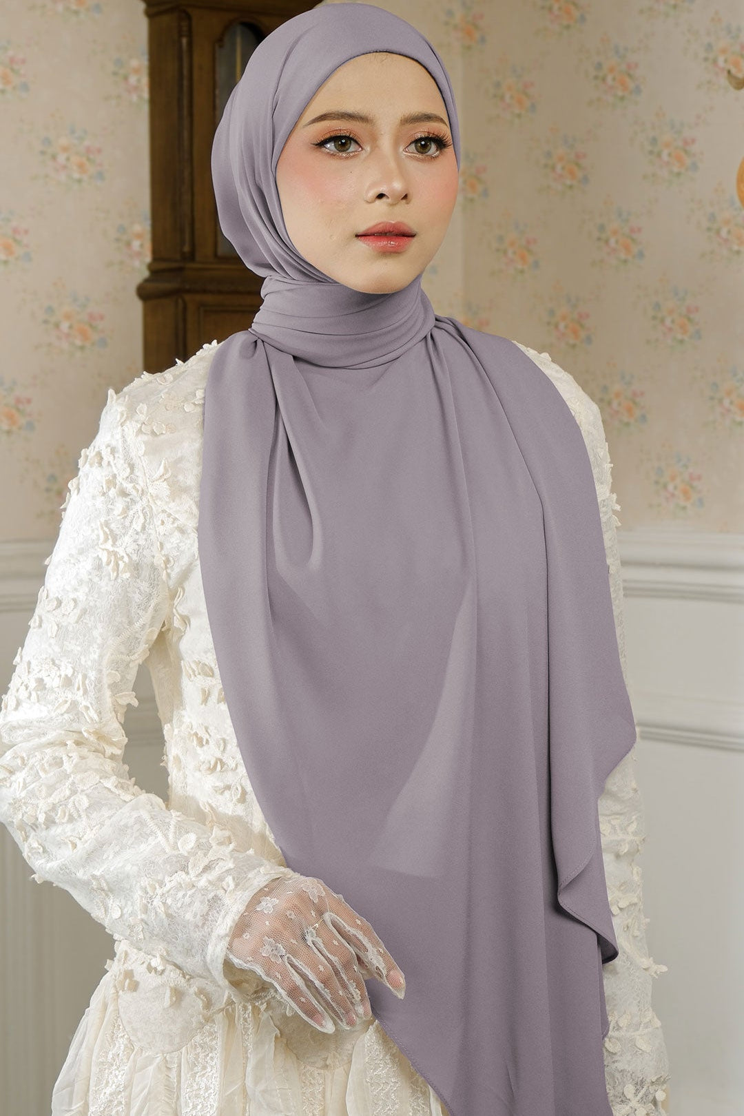 Woman wearing a light purple hijab and white gloves against a neutral background