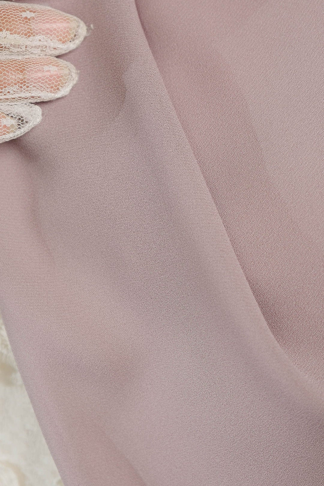 Close-up of a sheer fabric with lace trim on a soft pink background