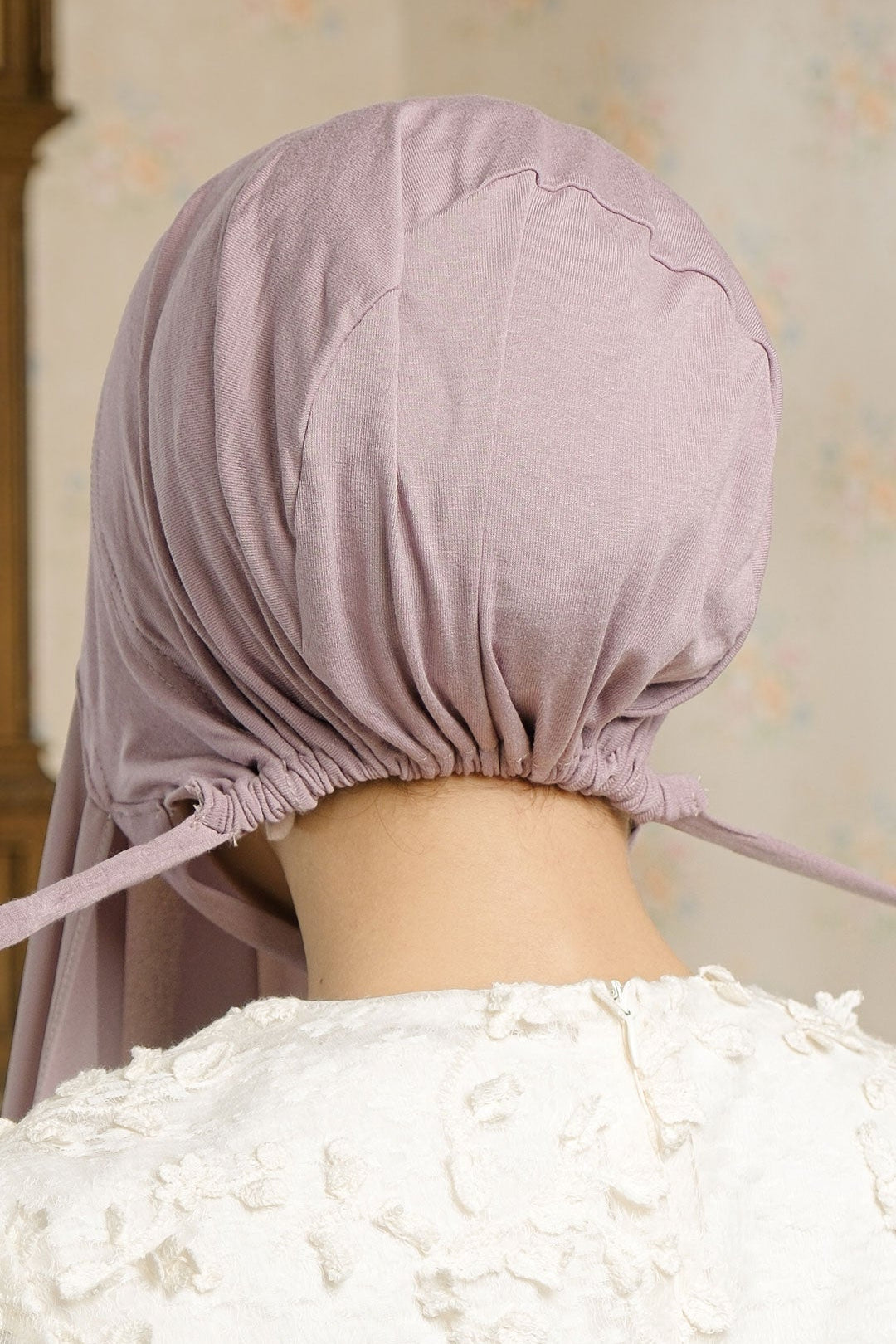 Person wearing a light purple headscarf with a neutral background