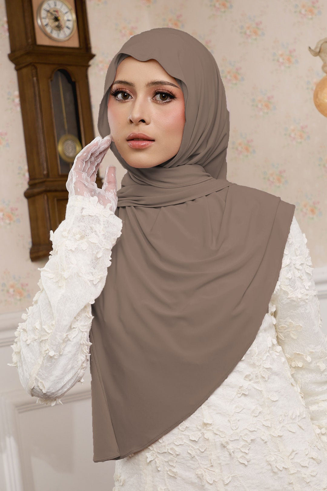Woman wearing a brown hijab and white gloves in a decorated room.