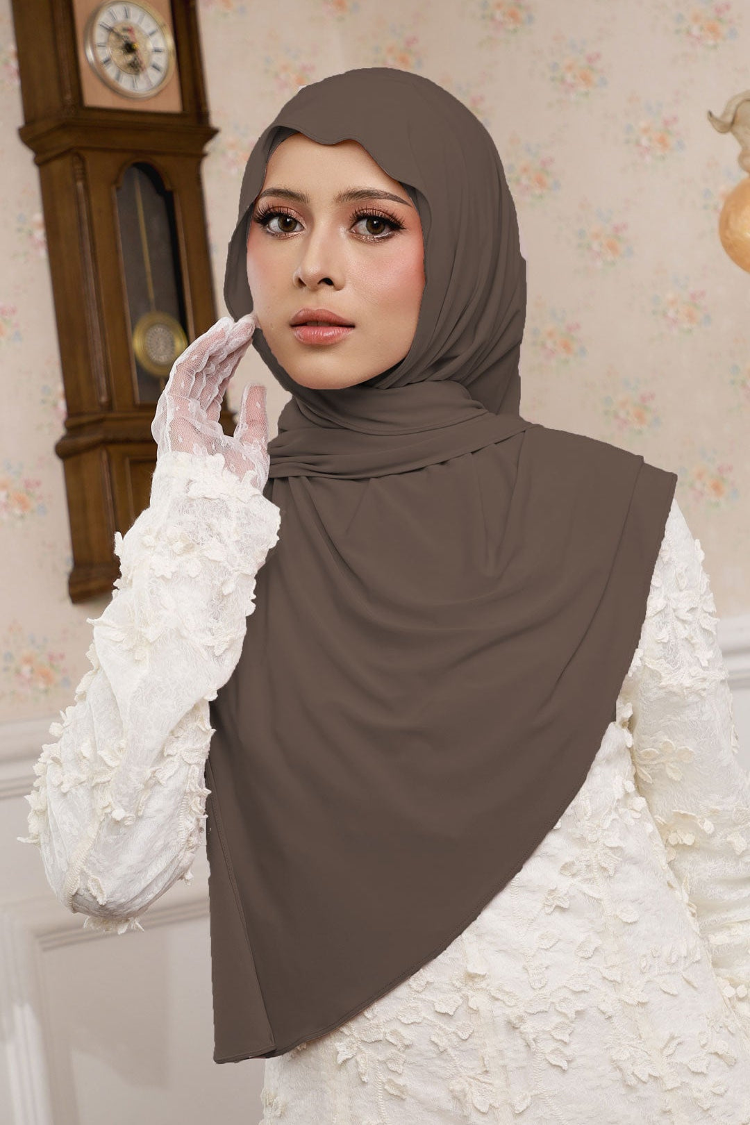 Woman wearing a brown hijab and white gloves in a decorated room.