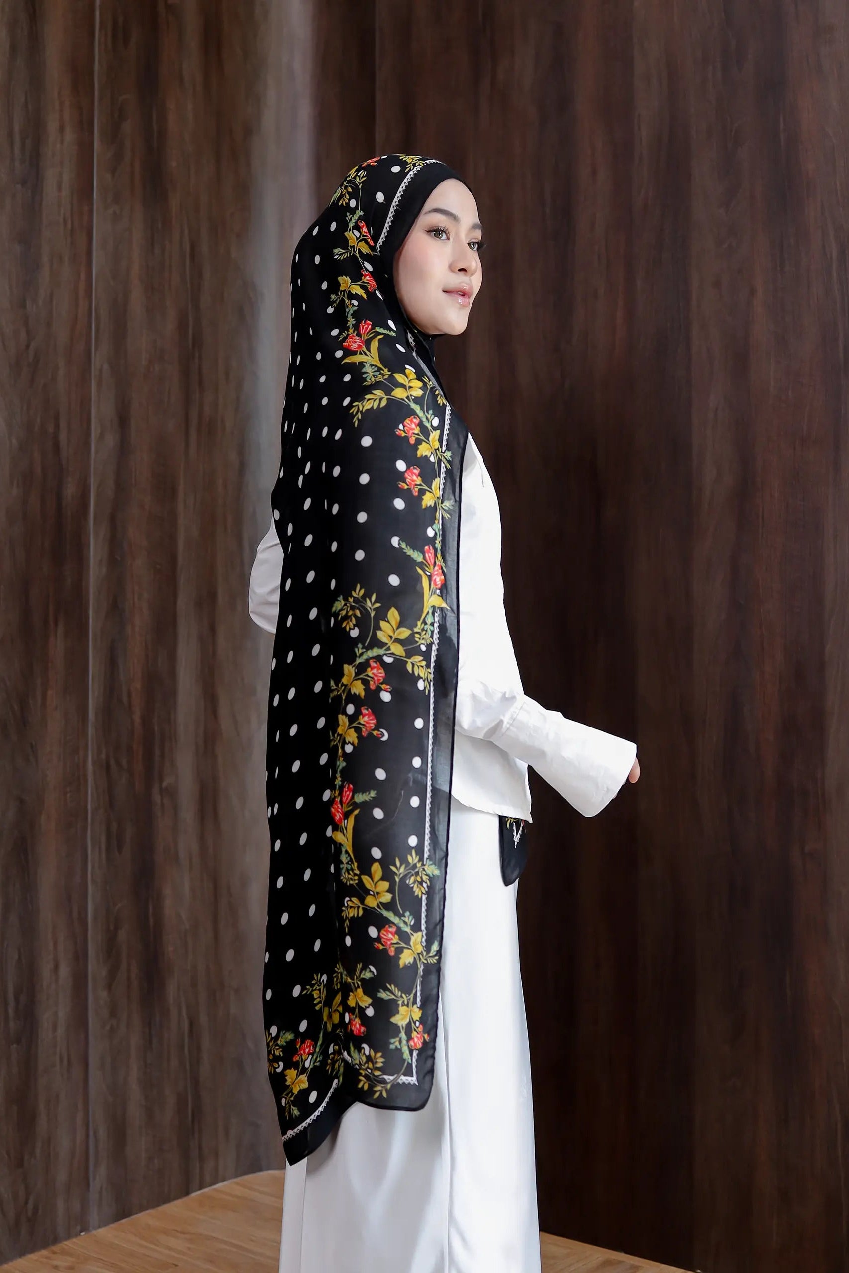 Woman wearing a black hijab with floral patterns against a wooden background