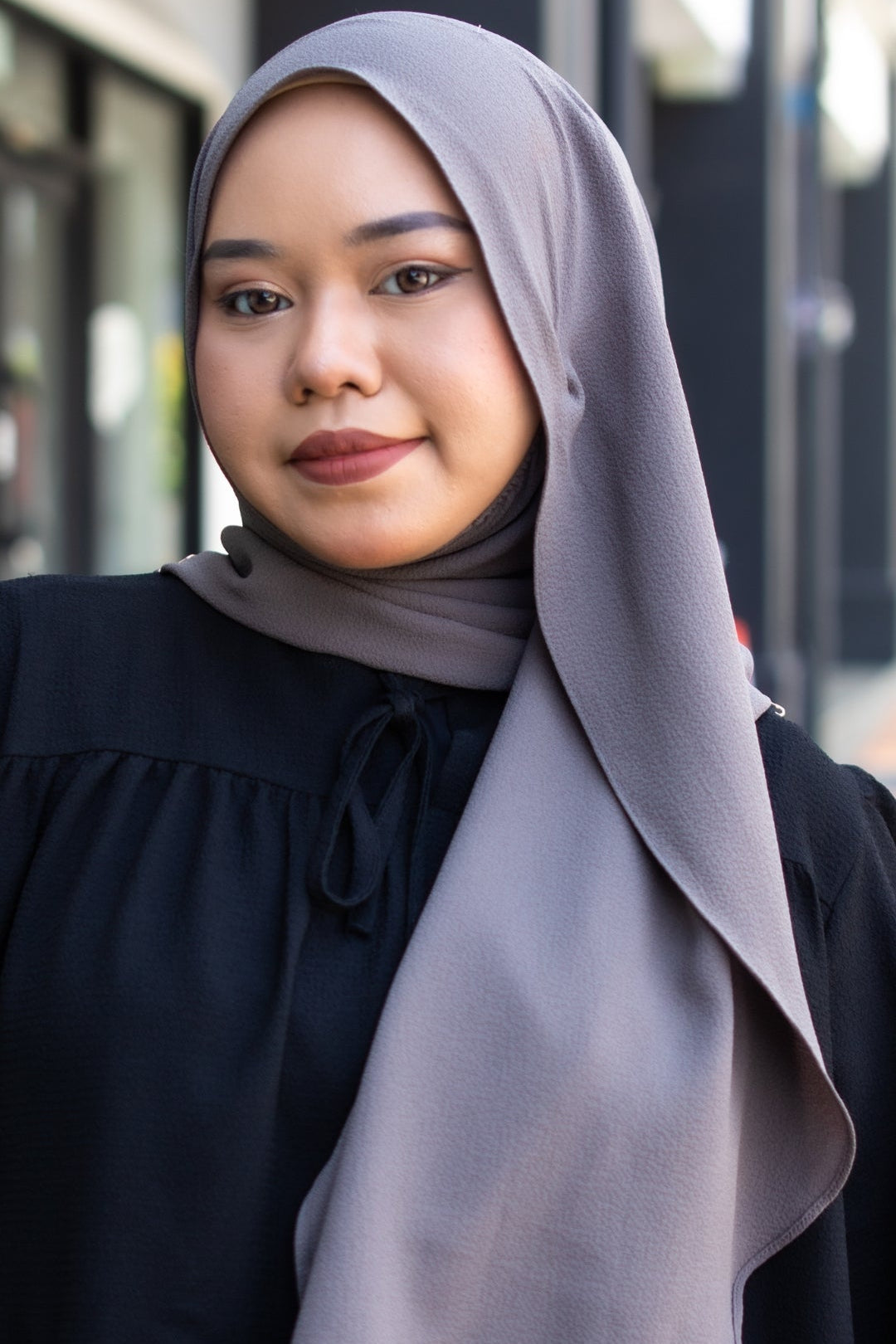 Woman wearing a gray hijab and black top outdoors