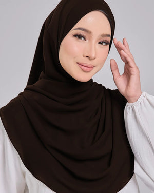 Woman wearing a brown hijab and white blouse against a gray background