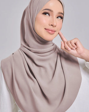 Woman wearing a beige hijab against a gray background