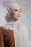 Woman wearing a beige hijab and brown top against a colorful abstract background