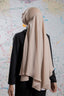 Person wearing a beige hijab and black outfit against a colorful abstract wall.