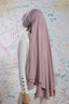 Person wearing a light pink hijab in front of a colorful abstract wall.