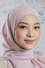 Woman wearing a light pink hijab against a patterned background