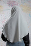 Person wearing a light gray hijab with black sleeves against a colorful abstract background