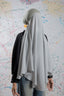 Person wearing a light gray hijab in front of a colorful abstract wall.