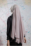 Person wearing a beige hijab and black top against a colorful abstract wall.