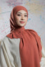 Woman wearing a rust-colored hijab against a colorful abstract background
